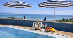 Piscina con vino, frutta e ombrelloni blu vista mare.