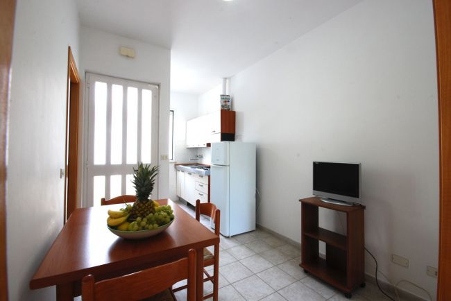 Cucina con tavolo da pranzo, TV e piatto di frutta.