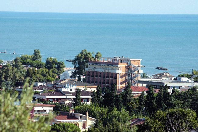 Vista su edifici e mare, circondati da alberi.