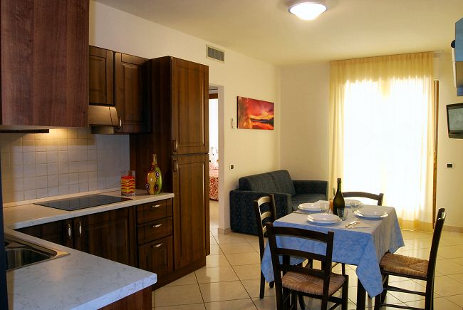 Cucina moderna con tavolo apparecchiato e divano in soggiorno luminoso.