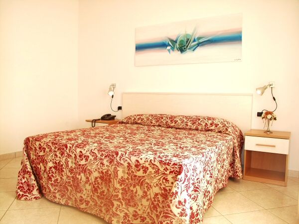 Letto matrimoniale con copriletto a motivi rossi.