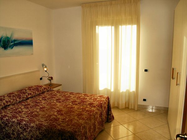 Camera da letto con letto matrimoniale, copriletto a motivi rossi e finestra luminosa.