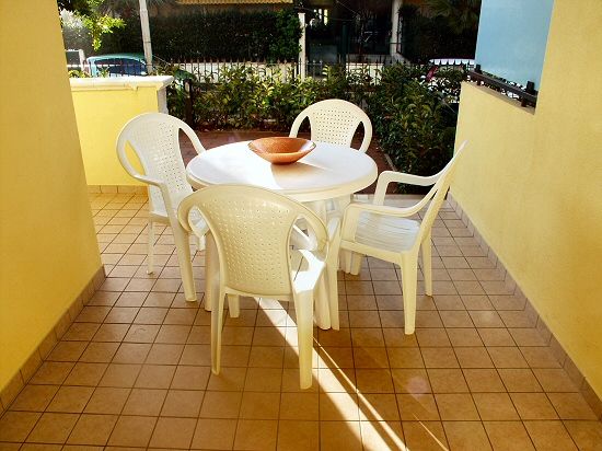 Un tavolo rotondo bianco con cinque sedie bianche su un patio piastrellato.