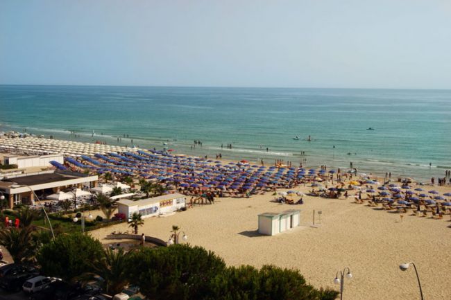 Spiaggia affollata con ombrelloni colorati vicino al mare.