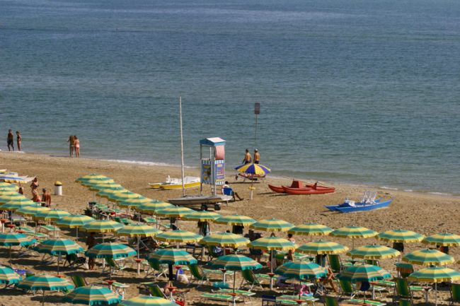 Spiaggia con ombrelloni verdi e gialli, lettini e alcune persone in riva al mare.