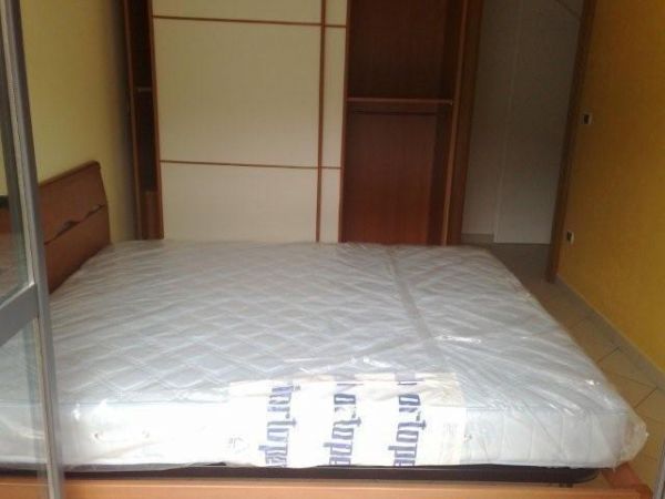 Un letto matrimoniale con materasso avvolto in plastica, davanti a un armadio.