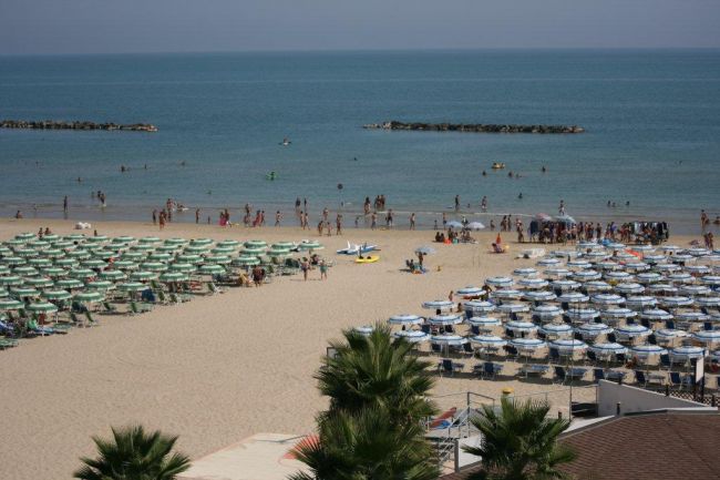 Una spiaggia affollata con lettini e ombrelloni vicino al mare calmo.