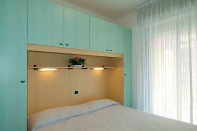 Camera da letto con armadio verde e tende bianche.