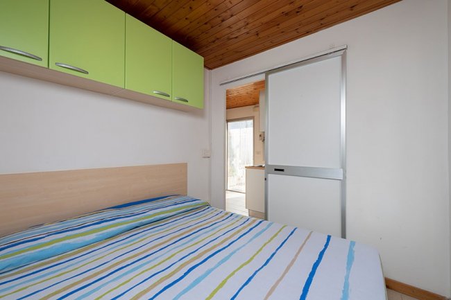 Camera da letto con armadio verde e letto con copriletto a righe.