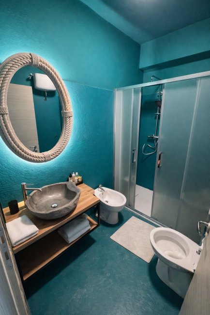 Bagno moderno con pareti turchesi e doccia a vetri.