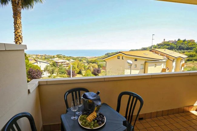 Vista dal balcone con tavolo e frutta, mare in lontananza.